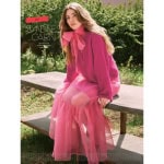 Sandnes Garn Einzelanleitung 2308-1 ARTISANE CARDIGAN, Frau in pinkem Strickkleid im Garten.