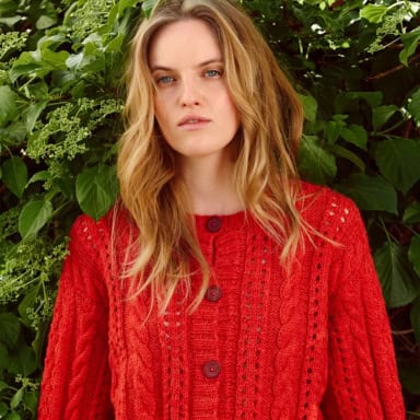 Sandnes Garn Cornelia Cardigan für Fortgeschritten, rotes Strickstück vor grüner Natur.