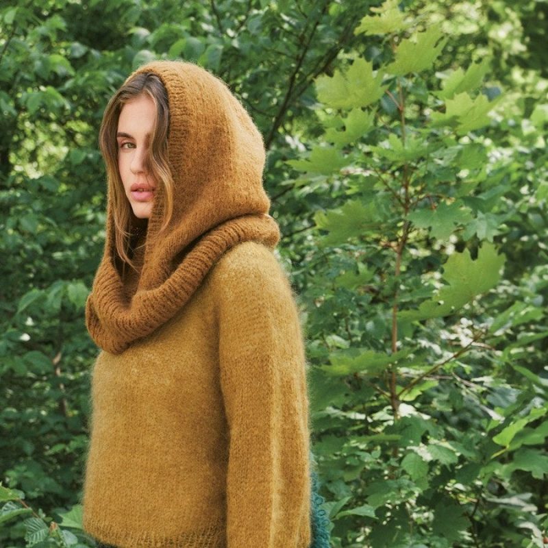 Sandnes Garn Einzelanleitung 2507-11 Snuggle Hood in Monochrom, getragen von einer Frau im Grünen.