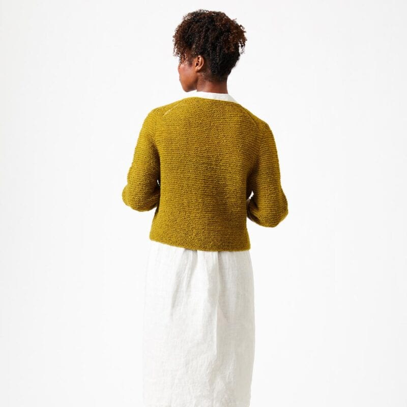 Frau trägt einen grünen, gestrickten Cardigan Zoe aus Wolle, Rückenansicht, Wollke-Shop.