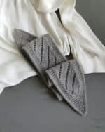 Ein gestrickter Schal aus grauem Garn liegt auf einem grauen Tisch neben einem weißen Hemd.