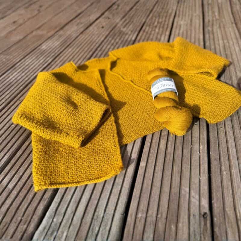 Gehäkelte gelbe Jacke aus Wolle, Garn und Häkelnadel, perfekt für das Stricken und Häkeln.