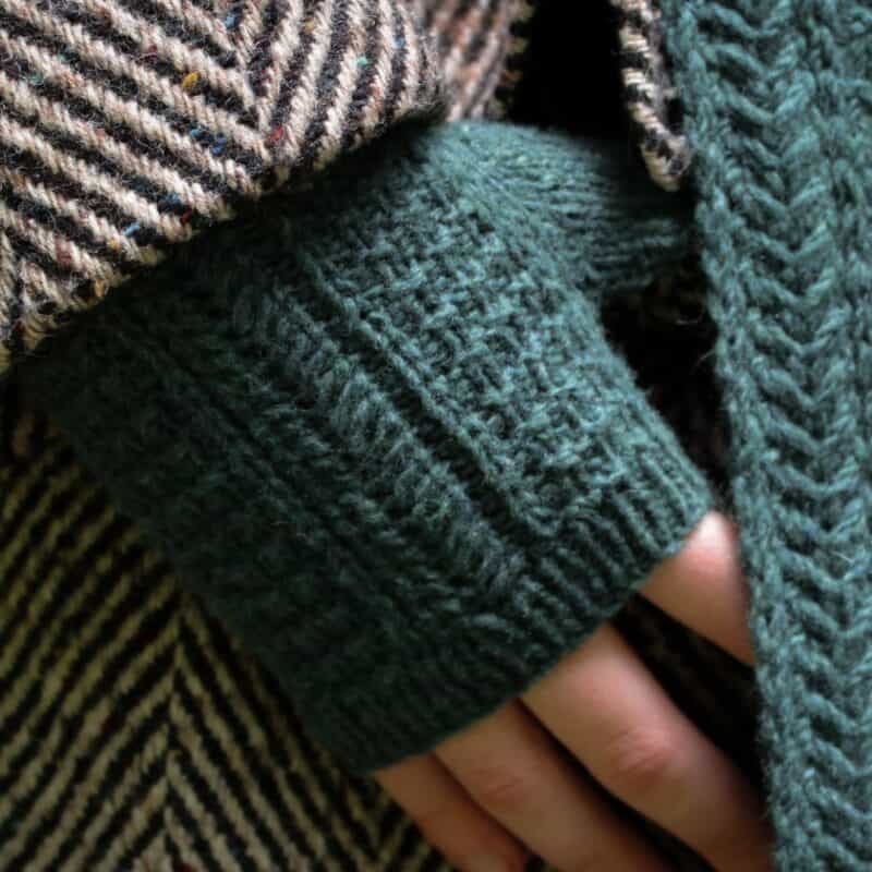 Strickset für ALYSSUM KERCHIEF mit Garn und Anleitung, zeigt eine handgestrickte Hand mit Wollhandschuhen.