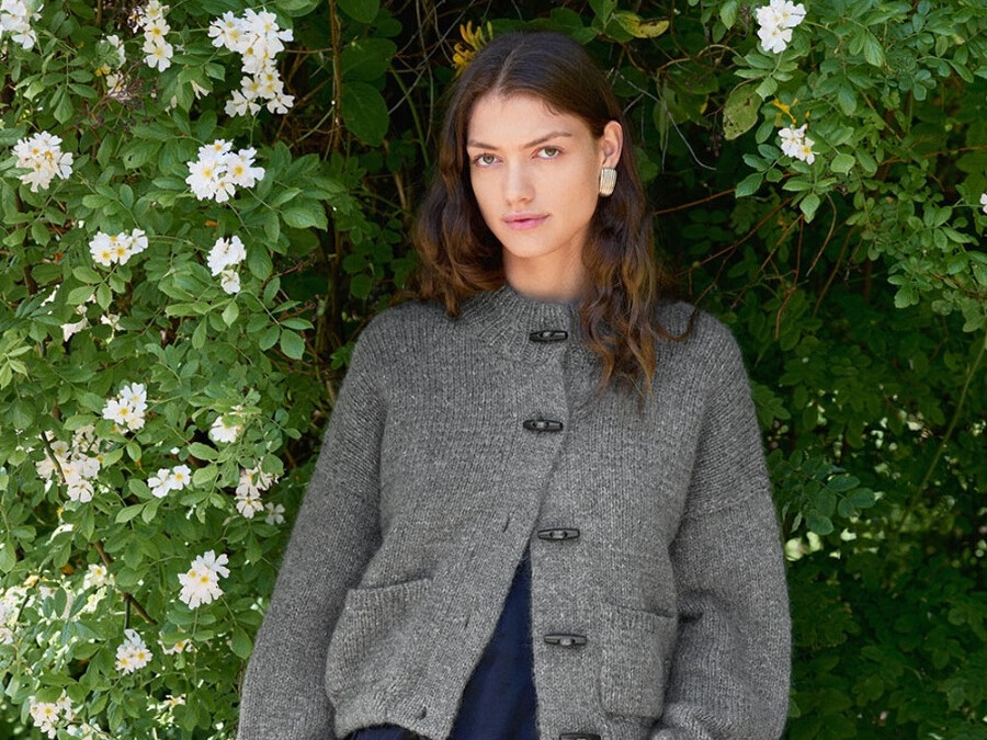 Gestrickte Bomber Jacket aus der Sandnes-Kollektion DIY 2606, getragen vor blühendem Grün.